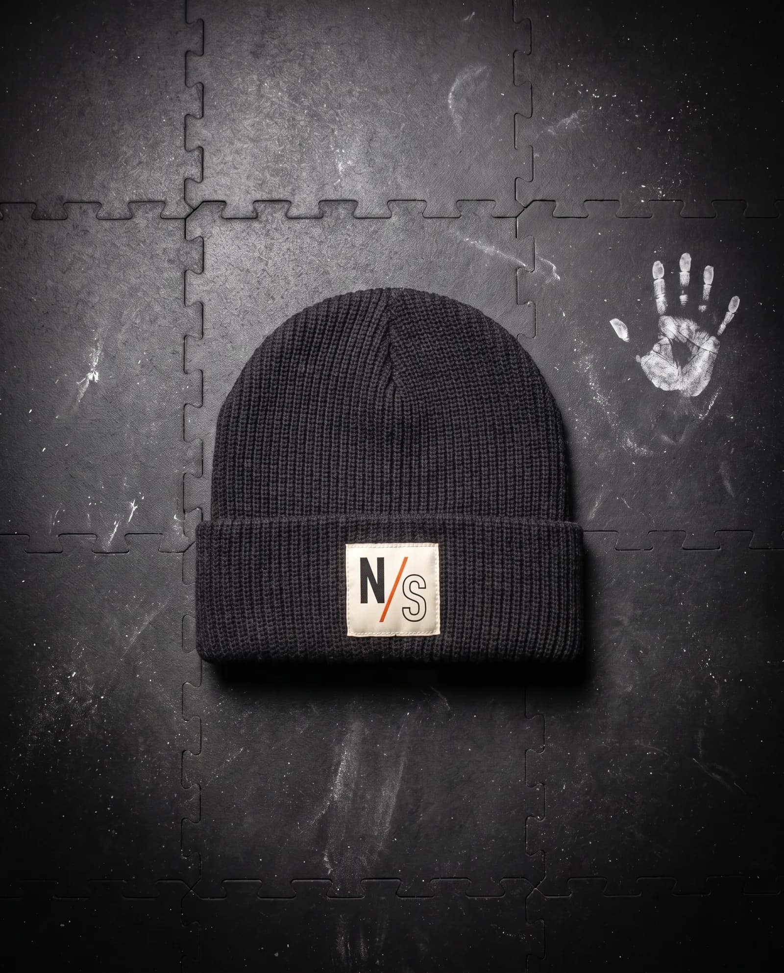 Cuff Beanie in Carbon, laid flat on a gym floor