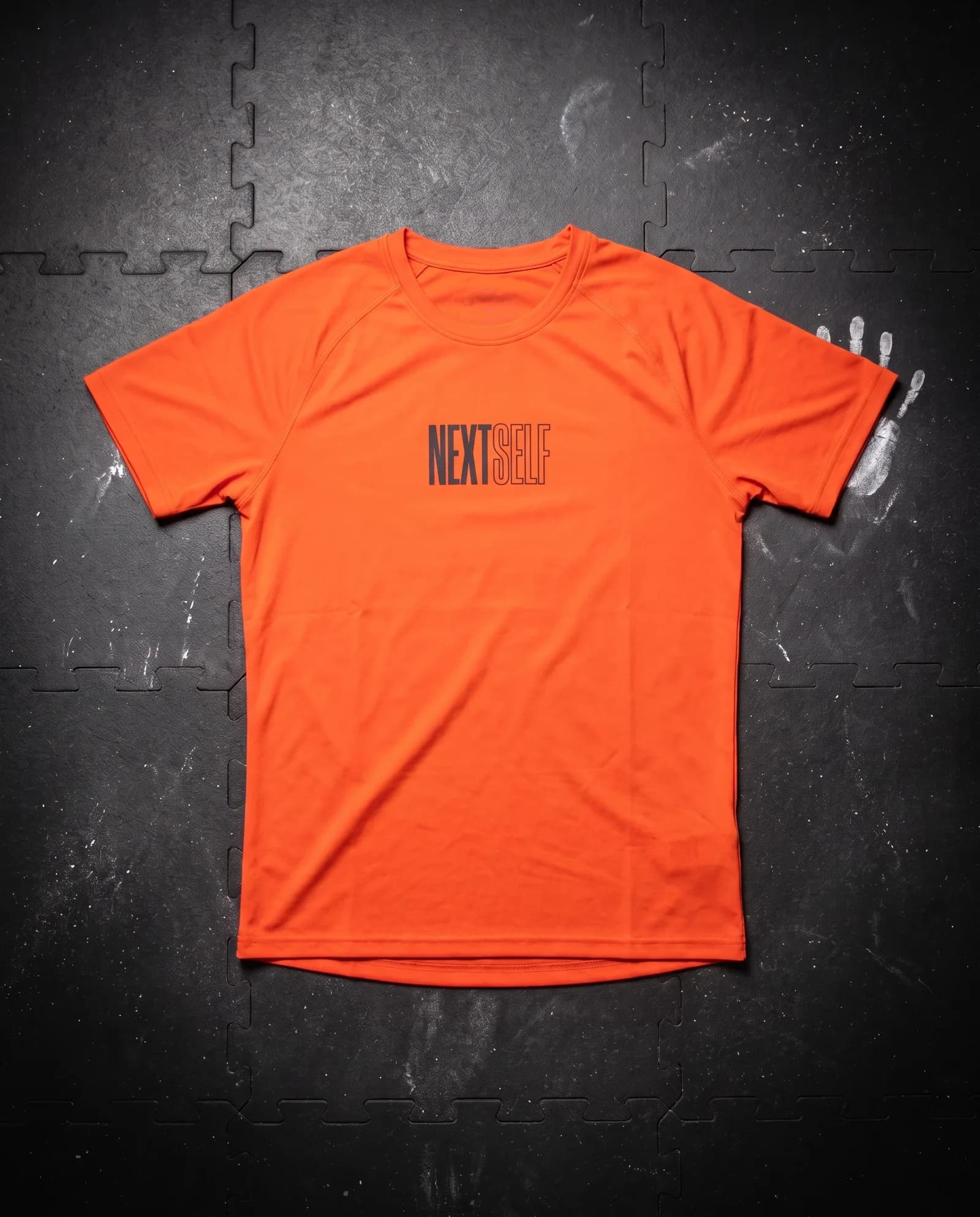 Rep Tee in Carbon, laid flat on a gym floor